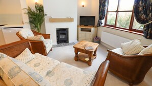 Una sala de estar acogedora con sofá, sillas, una mesa de centro, chimenea, televisor y una ventana con cortinas.