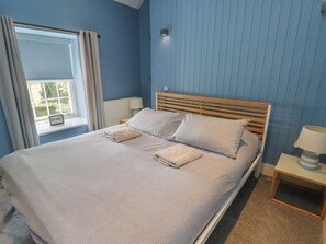 Un dormitorio con cama, mesita de noche, lámpara y ventana con cortinas.
