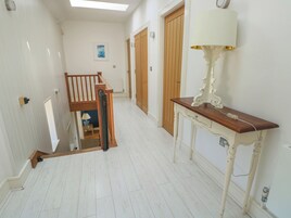 A hallway with white walls, a wooden staircase, and a table with a lamp.