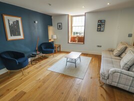 Un salón con pared azul, suelo de madera, sillón azul, sofá gris, una mesita y una ventana con vistas.