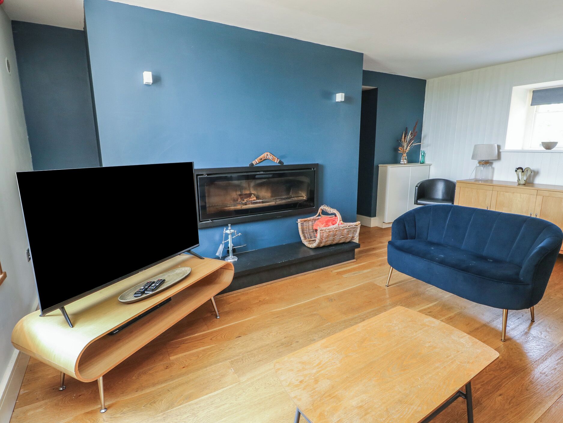 Un salon moderne avec un téléviseur à écran plat, une cheminée, un canapé bleu et une table basse en bois.