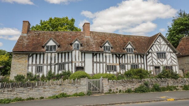 A traditional half-timbered building with multiple windows and a stone wall. - Coach House Mews (Stratford-upon-Avon)