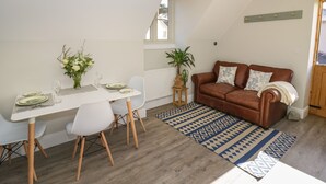 A dining area with a white table set for four, a brown leather sofa, and a patterned rug. - Coach House Mews (Stratford-upon-Avon)