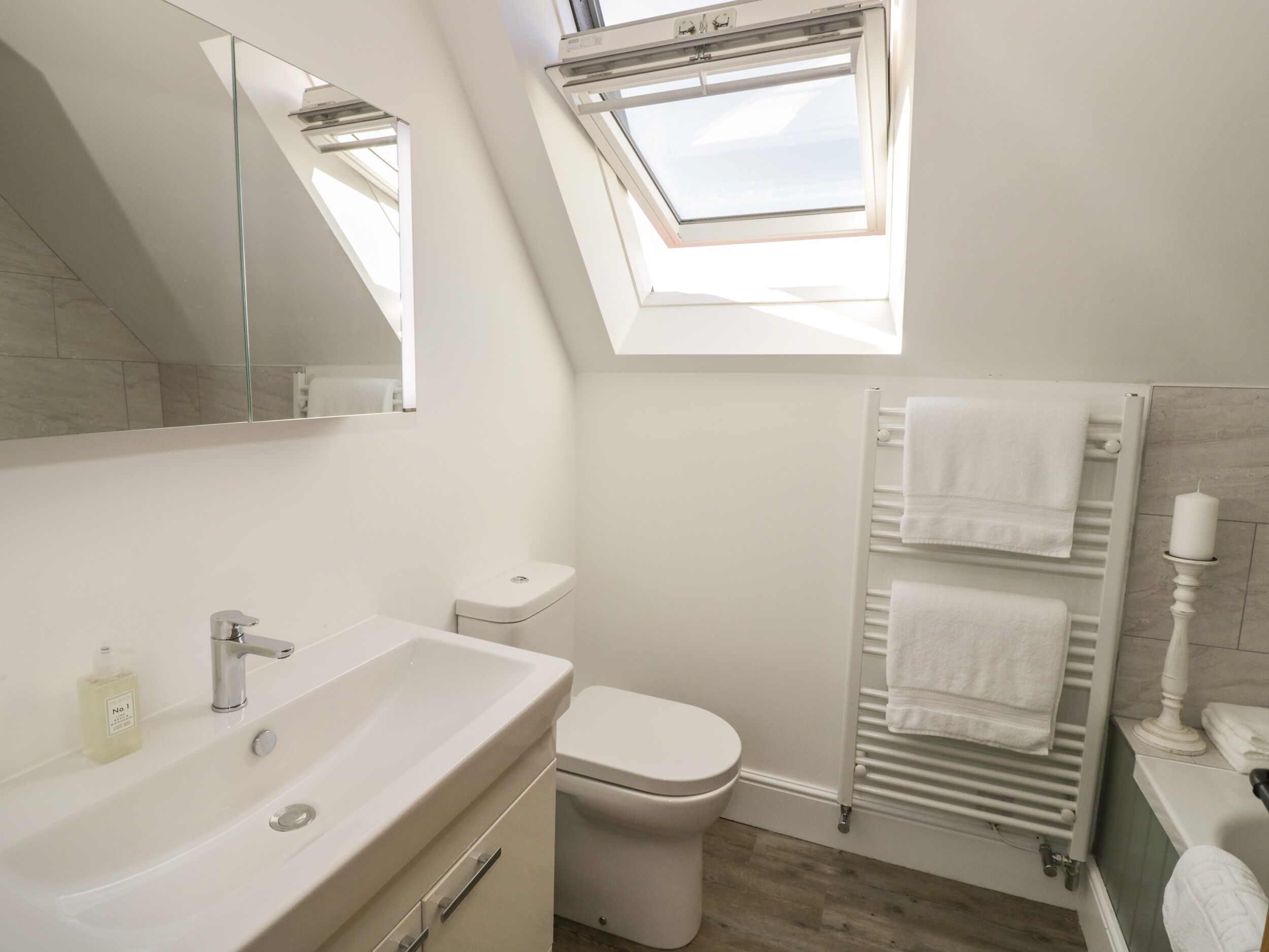 A modern bathroom with a skylight, a white sink, a toilet, and a towel rack.