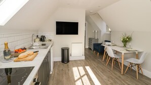 A modern kitchen with a dining area, a TV mounted on the wall, and a window providing natural light. - Coach House Mews (Stratford-upon-Avon)
