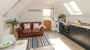 A cozy kitchen with a brown leather sofa, a dining table with plates, and a patterned rug. - Coach House Mews (Stratford-upon-Avon)