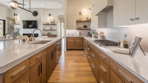 A modern kitchen with wooden cabinets, a large island, and a built-in stove. - Modern 3BR Parade Home - w/Casita & Putting Green (St. George)