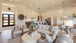 A spacious living room with a large sofa, a coffee table, and a dining area with chairs. - Modern 3BR Parade Home - w/Casita & Putting Green (St. George)
