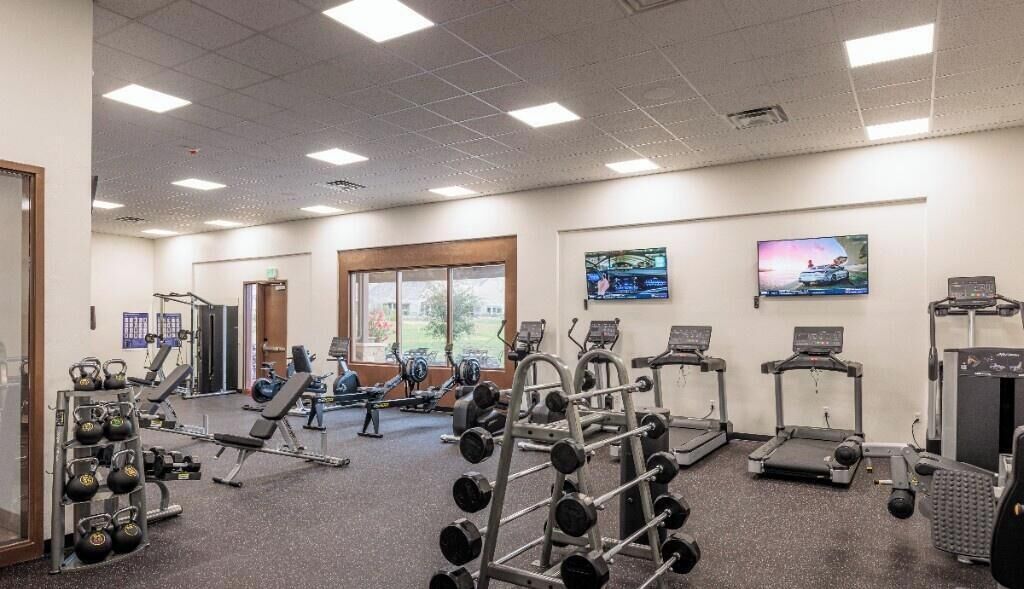 Ein Fitnessstudio mit verschiedenen Trainingsgeräten, darunter Laufbänder, Kraftgeräte und Kurzhanteln.