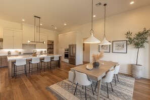 A modern kitchen with white cabinets, stainless steel appliances, and a wooden dining table with bar stools.