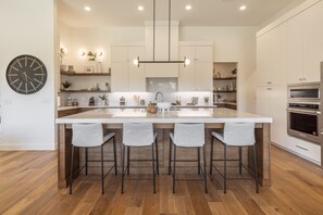 A modern kitchen with a central island, bar stools, built-in appliances, and a clock on the wall.