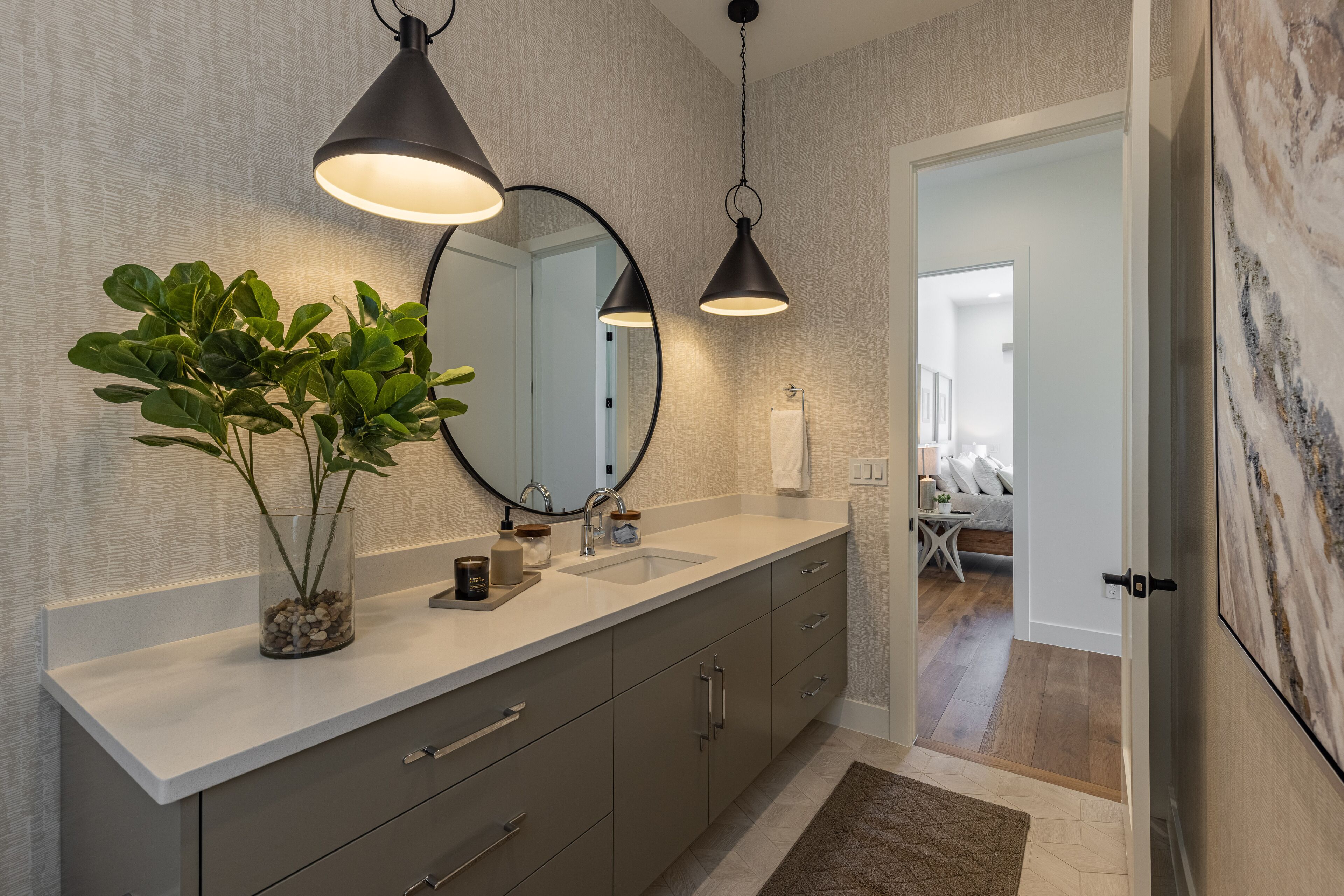 A modern bathroom with a large mirror, two pendant lights, a sink, and a potted plant.