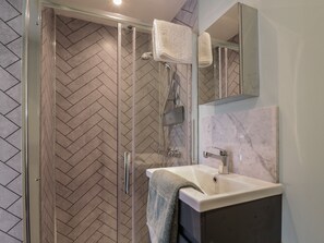A modern bathroom with a herringbone tile floor, a glass shower enclosure, a white sink, and a mirror above the sink. - Coastguards View (Herne Bay)