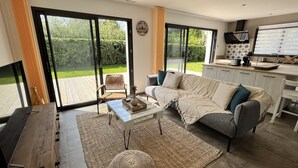 A modern living room with a sofa, coffee table, and a view of a garden through large sliding doors. - DEGEMER MAT! Cosy, Modern, 8 minutes from the beach (Moëlan-sur-Mer)