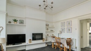 Una sala de estar con televisor de pantalla plana, candelabro, mesa de comedor con sillas y chimenea.