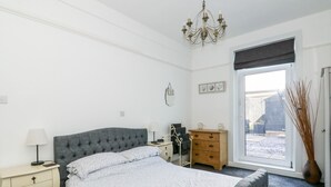 Un dormitorio con una cama grande, mesitas de noche, un aparador, una araña y una ventana con vistas al exterior.