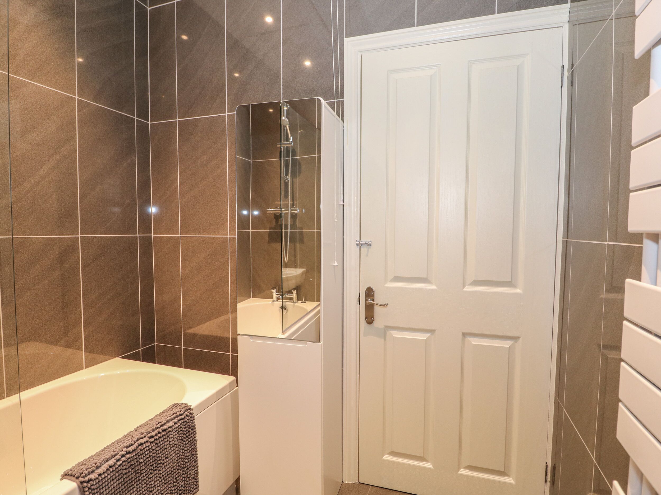 A bathroom with a bathtub, a mirror, and a white door.