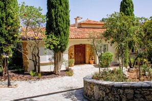 Une cour avec un chemin de pierre menant à un bâtiment doté d’un toit en tuiles et d’une porte en bois.