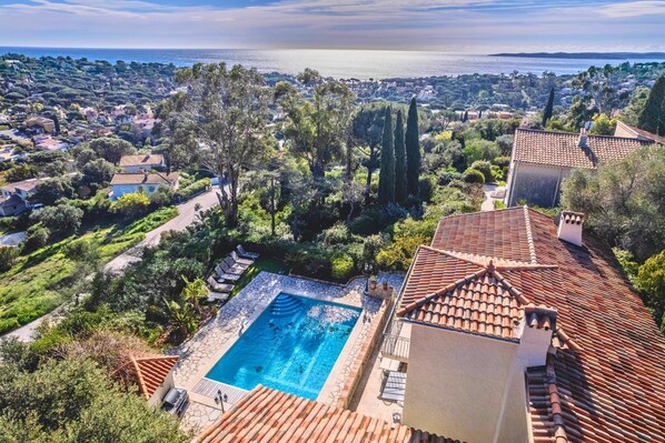 A residential area with a swimming pool, terracotta roofs, and a view of the sea.