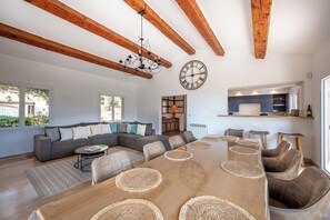 Un vaste espace de vie comprenant une grande table à manger en bois, un canapé d’angle gris et un lustre.