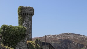 Una torre de piedra cubierta de hiedra, con montañas al fondo.