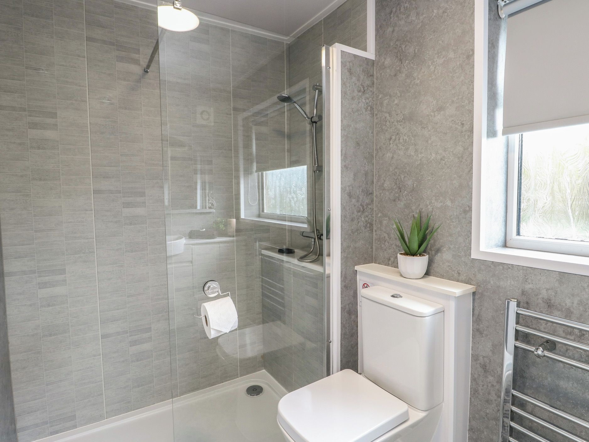 A modern bathroom with a glass-enclosed shower, a toilet, and a window.