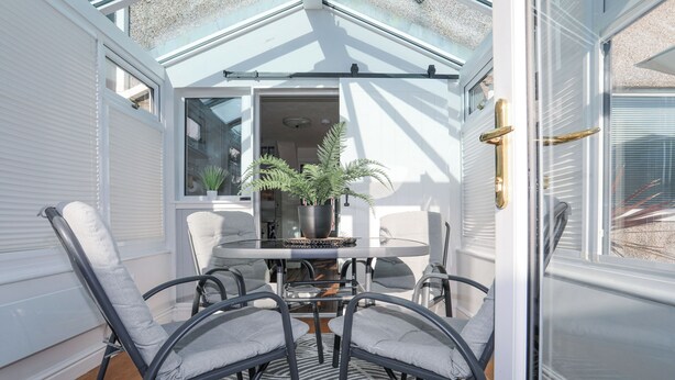 A sunlit room with a round table, four chairs, and a potted plant. - Glasfryn (Holyhead)