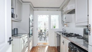 A narrow kitchen with white cabinetry, a built-in oven, a stove, and a washing machine. - Glasfryn (Holyhead)