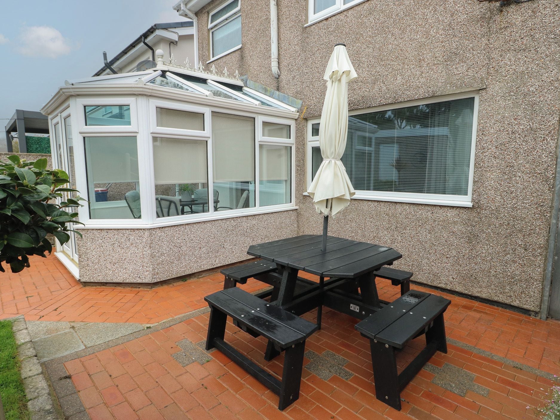 Une terrasse avec une table et des bancs, un espace salon couvert et une maison dotée d’une véranda.
