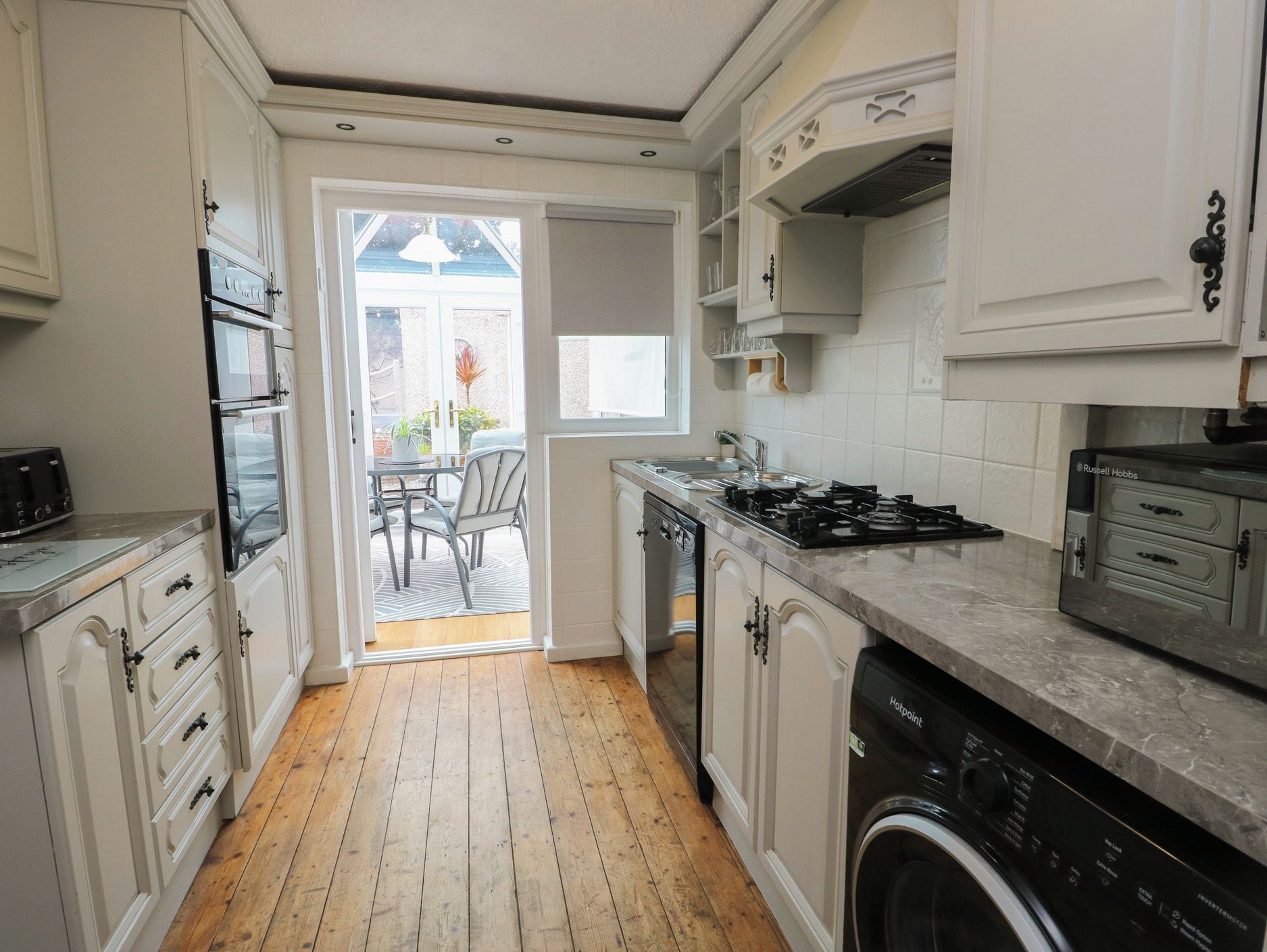 A compact kitchen with a dishwasher, stove, and a view to a patio area.
