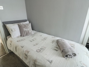 Una cama individual con una colcha a rayas y dos almohadas, una con un nombre bordado.
