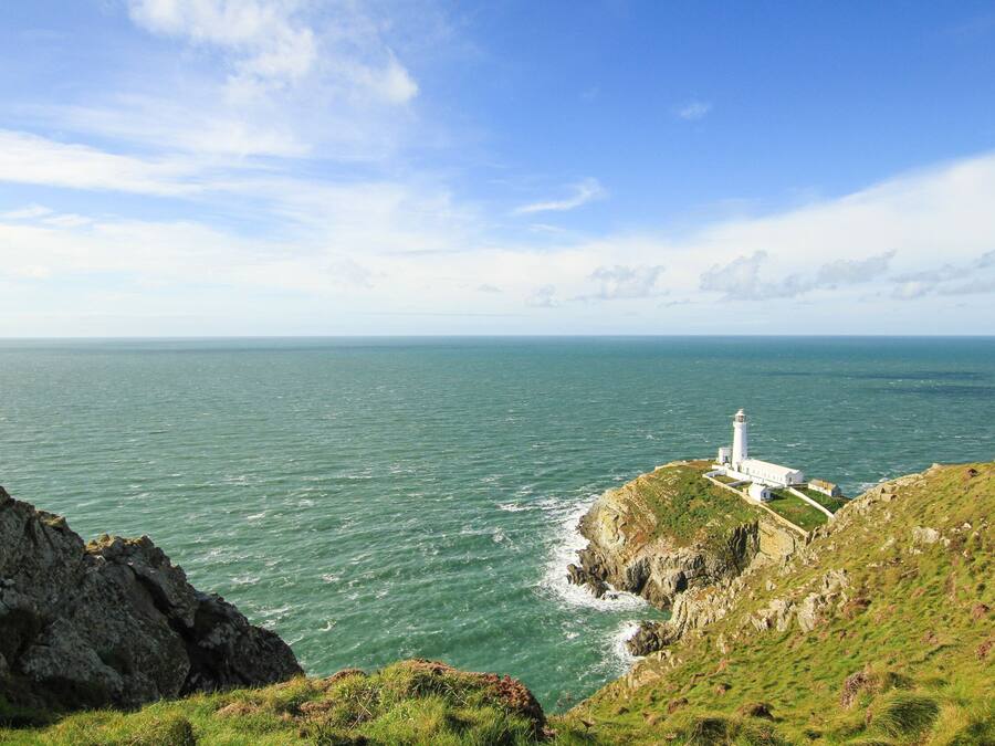 A coastal view with a lighthouse on a grassy cliff overlooking the sea.