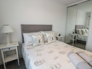 Un dormitorio con cama, mesitas de noche, lámpara, espejo y armario.