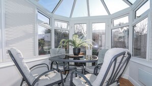 A conservatory with a glass ceiling, a round table, four chairs, and a potted fern. - Glasfryn (Holyhead)