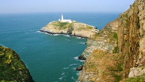 Un paisaje costero con un faro sobre un promontorio rocoso, con vista al mar.