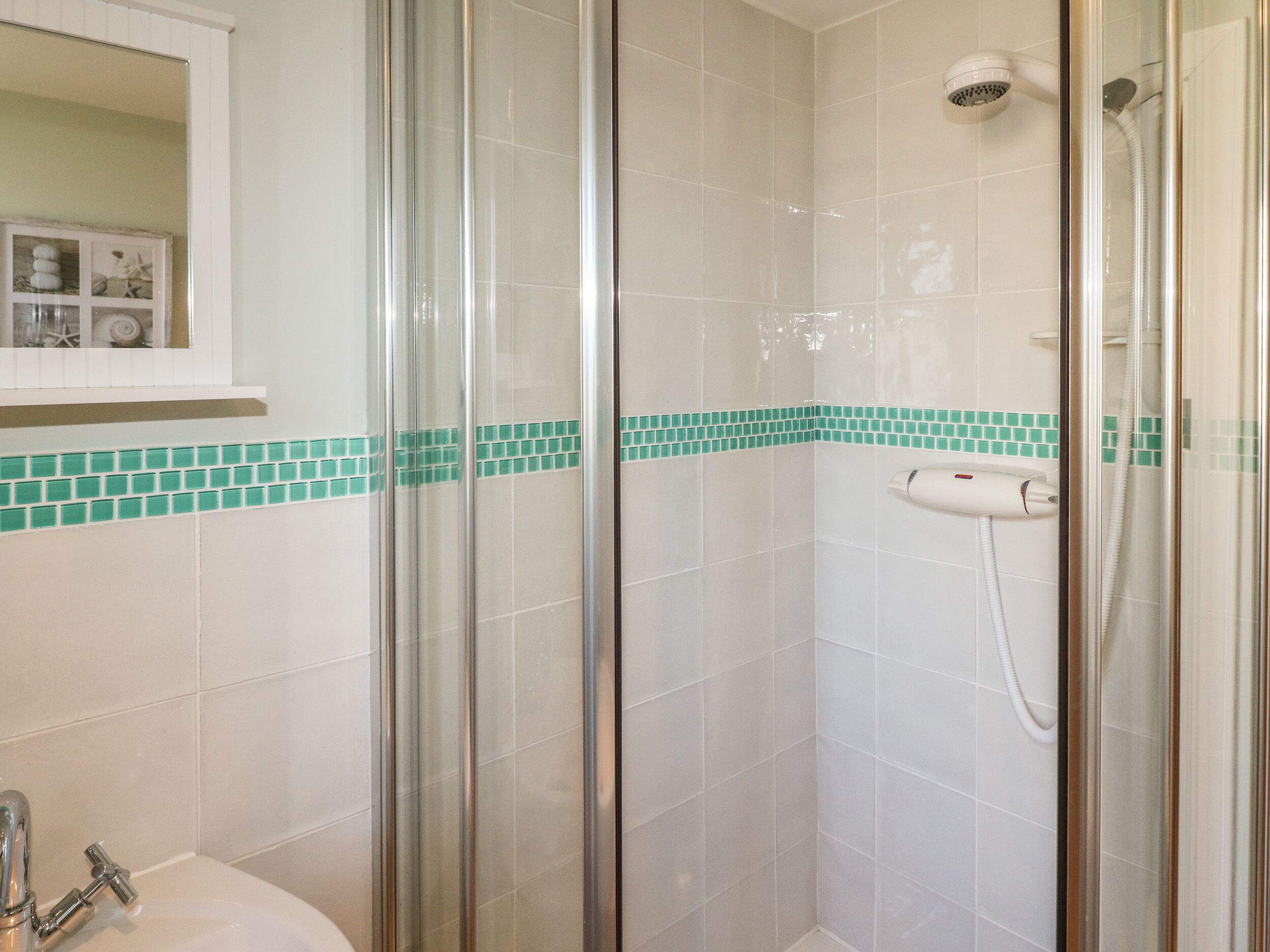 Un baño con cabina de ducha de vidrio, un lavabo blanco y un espejo sobre el lavabo.