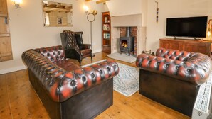A living room with a fireplace, leather sofas, a television, and wooden beams on the ceiling. - Chevin View (Belper)