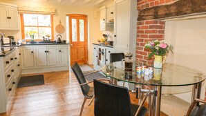 A kitchen with white cabinets, a glass dining table, and a brick fireplace. - Chevin View (Belper)