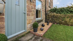 A stone building with a light blue door and windows, a small garden with a potted plant and decorative spheres, and a stone wall with ivy. - Chevin View (Belper)