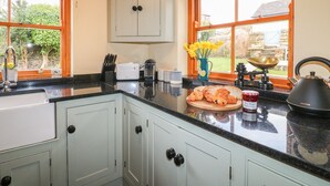 A kitchen with a black countertop, white cabinets, and a window with a view of a garden. - Chevin View (Belper)