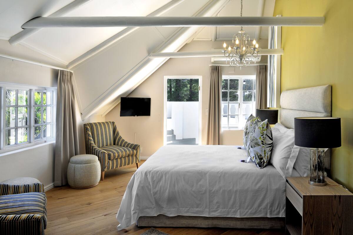 A bedroom with a large bed, a chair, a TV, and a chandelier.