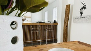 A wooden dining table with a white bowl, two clear chairs, and a wooden post in a modern interior with a wooden slatted wall and a framed picture on the wall. - Mirabelle Guesthouse (Franschhoek)