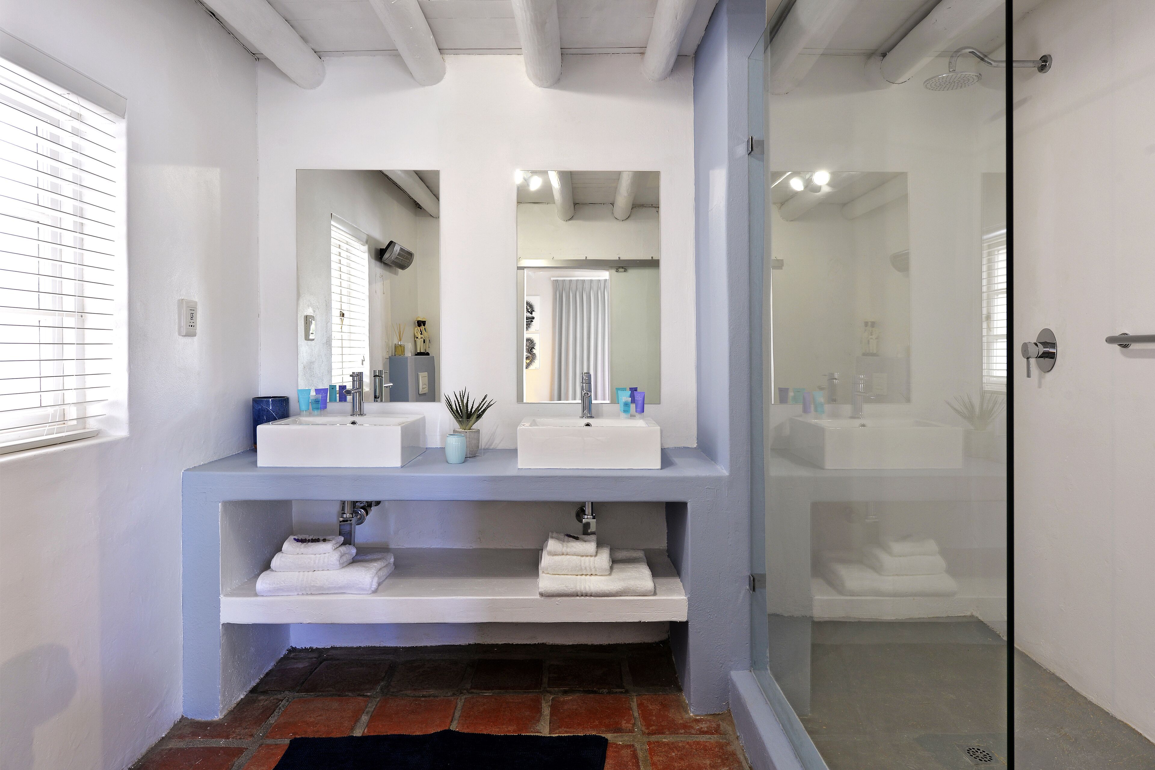 A bathroom with two sinks, a shower, and a glass door.