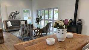 A modern living room with a wooden coffee table, two patterned armchairs, a sofa, and a large window with a view of greenery. - Mirabelle Guesthouse (Franschhoek)