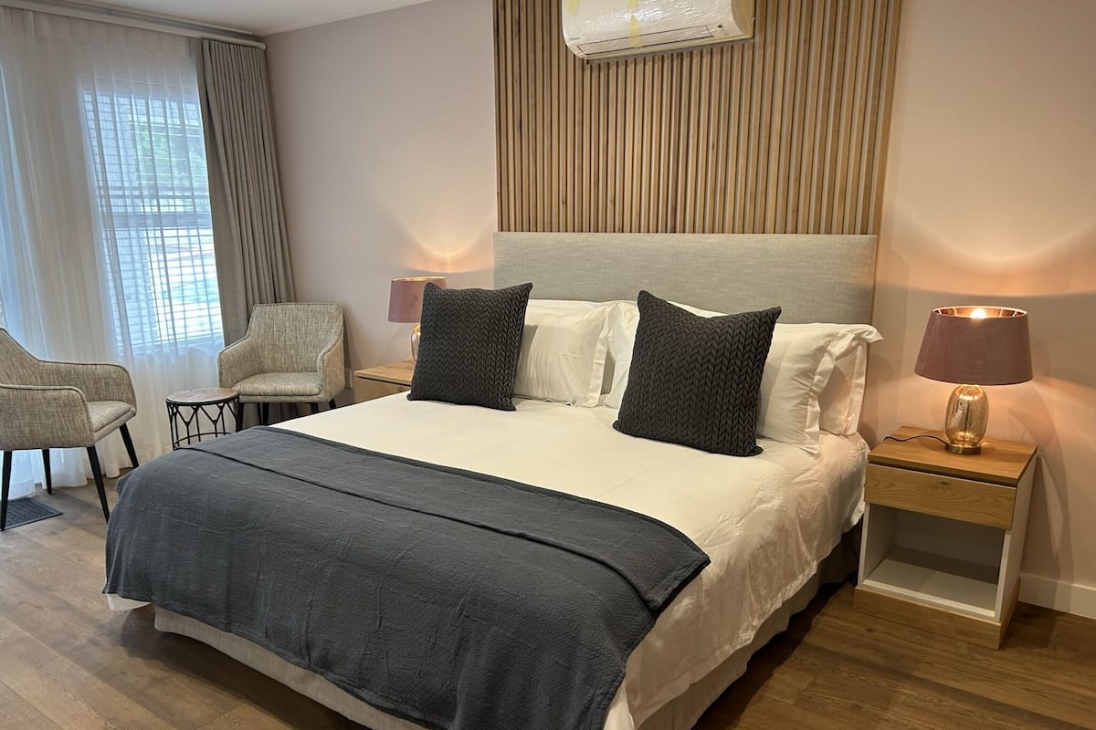 A modern hotel room with a large bed, two bedside tables, a chair, and a window with curtains.