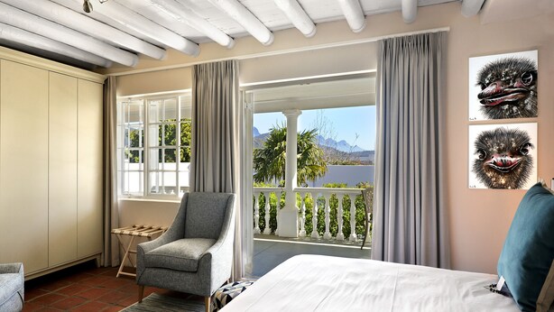 A bedroom with a large bed, a chair, a view of the outdoors, and artwork on the wall. - Mirabelle Guesthouse (Franschhoek)