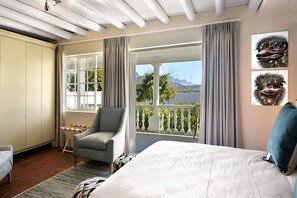 Une chambre avec un lit, une chaise, un balcon avec vue et des œuvres d’art accrochées au mur.