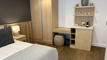 A modern bedroom with a bed, bedside table, lamp, wardrobe, and built-in desk with shelves.