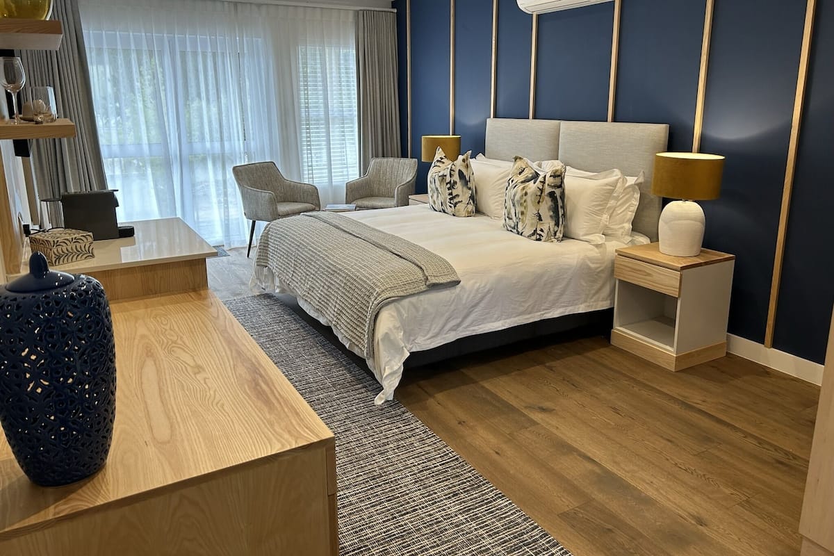 A modern hotel room with a large bed, a bedside table with a lamp, a chair, and a decorative vase.