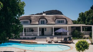 A large house with a swimming pool, lounge chairs, and a mountain in the background. - Mirabelle Guesthouse (Franschhoek)